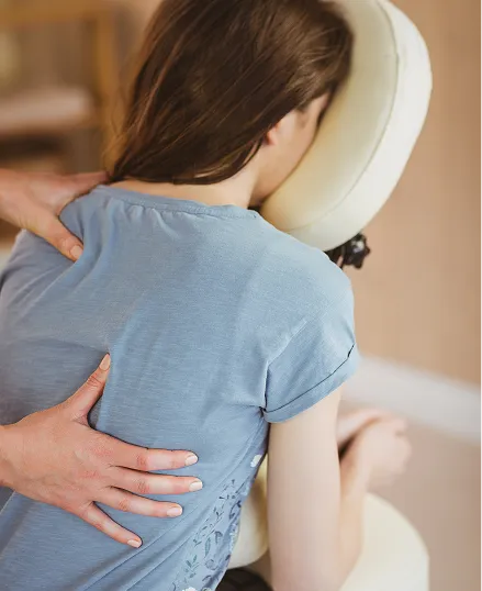 A person receiving a chair massage, with their arm wrapped around the back of a white chair and their head resting on the armrest.
