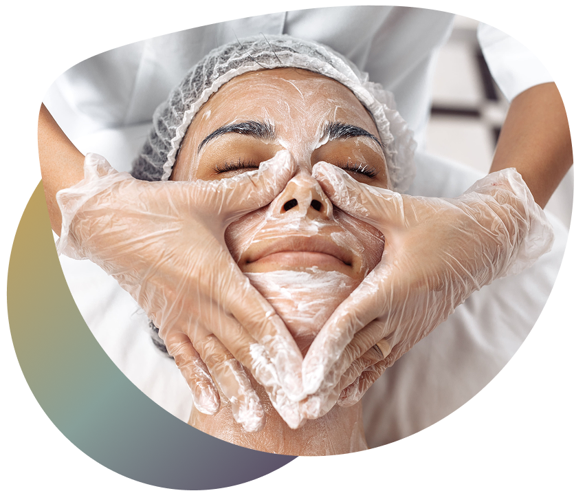A person receiving a facial treatment with a layer of white cream on their face, being treated by a professional in a spa-like setting.