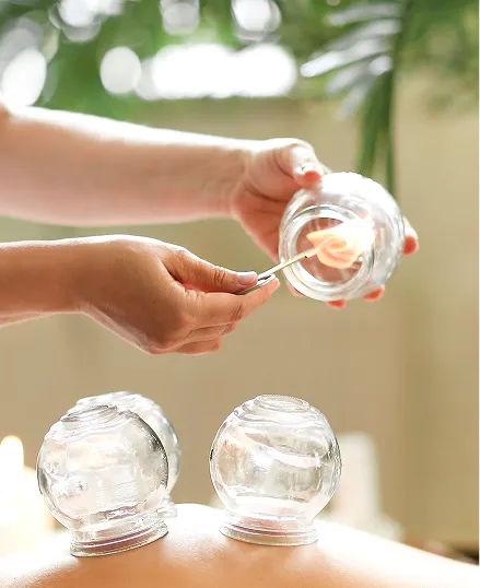 A person receiving a dry cupping massage treatment on their back, with a hand holding a small container filled with a pink flower.