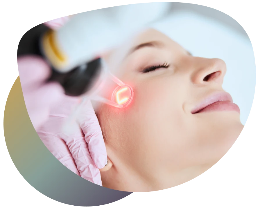 Woman undergoing facial treatment with red light device, wearing gloves, in a professional setting