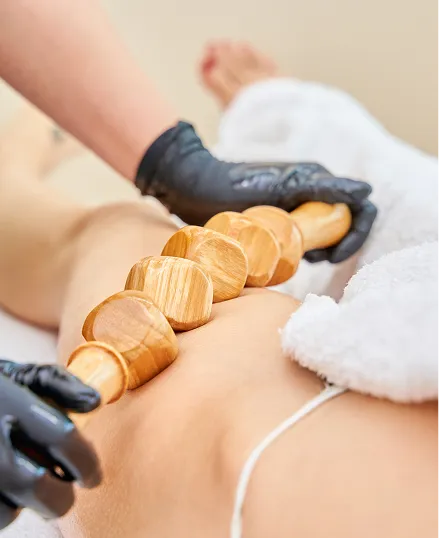 Woman receiving a massage on her back with wooden paddles, a professional massage therapist in black gloves is massaging her back.