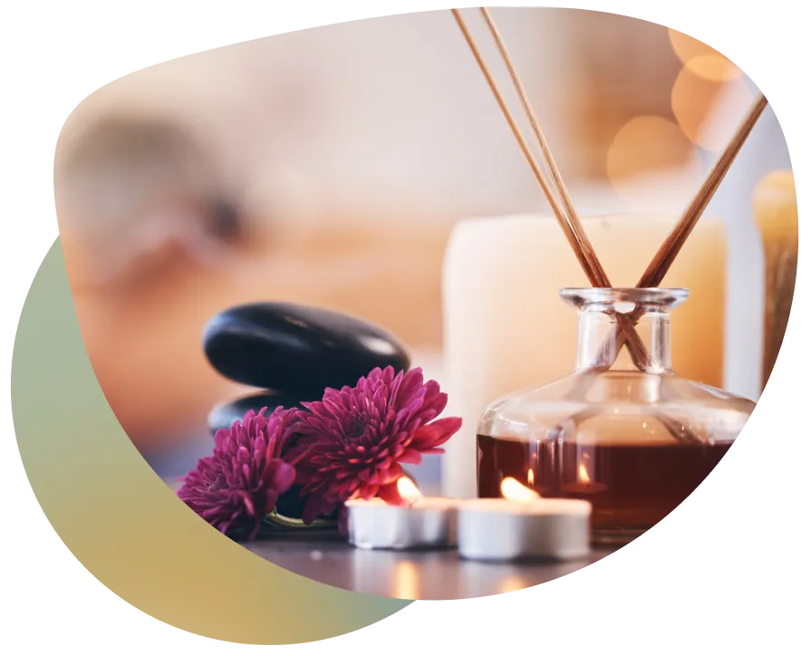 A serene table setting with a glass bottle of soap, a vase of pink flowers, and a lit candle, creating a peaceful atmosphere.