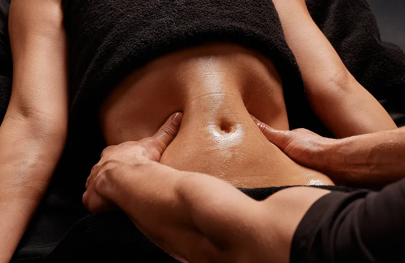 A person receiving a back massage, with a therapist's hands applying massage cream to their back, in a professional setting.