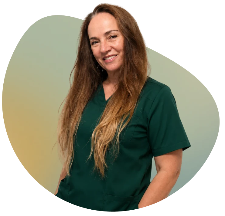 Woman in green surgical scrubs with long blonde hair and a welcoming smile, positioned against a white background.