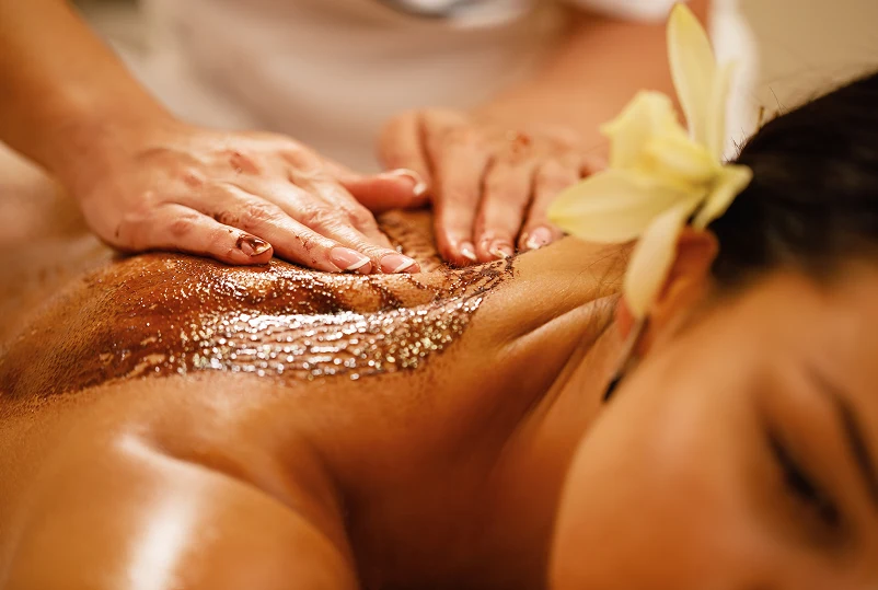 Woman receiving a massage with a gold face mask, in a spa setting, promoting relaxation and wellness.